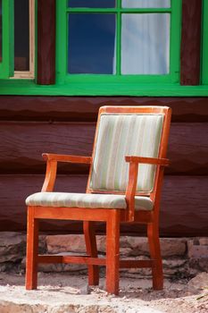Rustic chair outside log cabin with green window