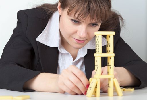 The young girl in black concentrated builds on a table a tower of dominoes