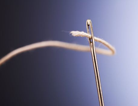 White thread going through needle eye, closeup