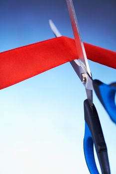 Closeup image of scissors cutting a red ribbon