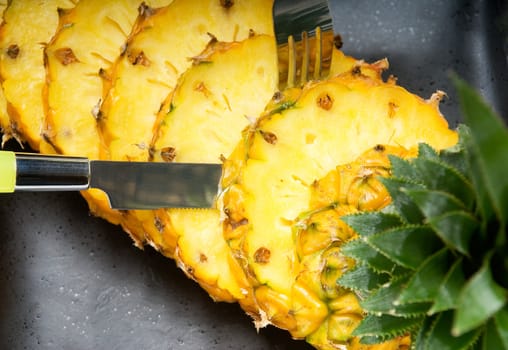 ripe vibrant pineapple sliced on a black plate with knife and fork