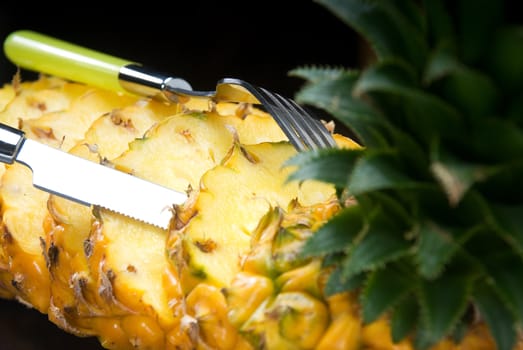 ripe vibrant pineapple sliced on a black plate with knife and fork