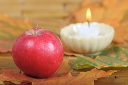 Red apple on autumn leaves with burning candle on a background