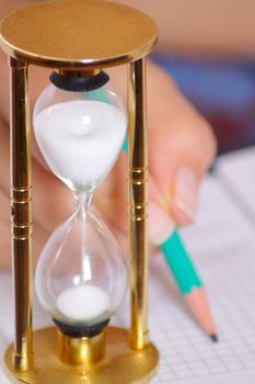 Sand-glass with female hand holding pencil on background