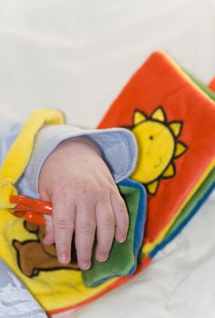 Hand from five months old baby playing with colorful book made from fabric - vertical