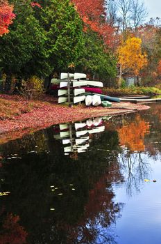 Canoes at forest of colorful autumn trees reflecting in calm lake