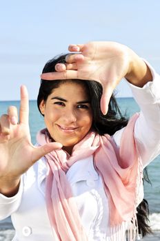 Portrait of beautiful smiling brunette girl framing her face at beach