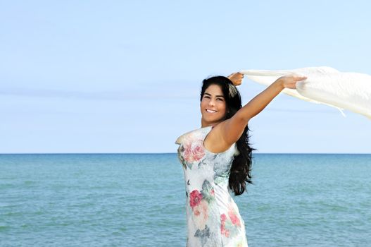 Portrait of beautiful smiling brunette girl at beach with arms outstretched