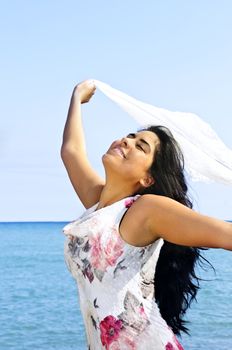 Portrait of beautiful smiling brunette girl at beach holding white scarf