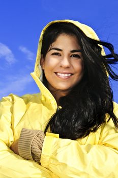 Portrait of beautiful smiling brunette girl wearing yellow raincoat against blue sky