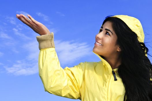 Portrait of beautiful smiling girl wearing yellow raincoat looking up checking for rain