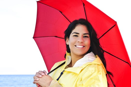 Portrait of beautiful smiling brunette girl wearing yellow raincoat holding red umbrella