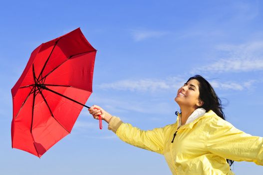 Portrait of beautiful girl wearing yellow raincoat holding red umbrella on windy day