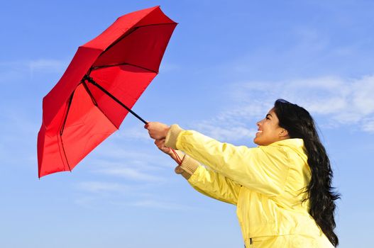 Portrait of beautiful girl wearing yellow raincoat holding red umbrella on windy day