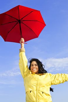 Portrait of beautiful girl wearing yellow raincoat holding red umbrella on windy day