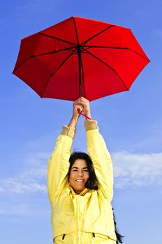 Portrait of beautiful girl wearing yellow raincoat holding red umbrella on windy day