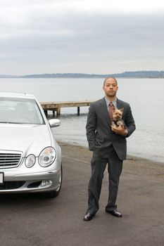 Ethnic Business Man and Yorkshire Terrier Dog are standing next to the lake. He is dressed in a suit and tie and is holding the dog.