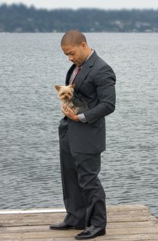 Ethnic Business Man with his Yorkshire Terrier Dog standing on a pier next to the lake.