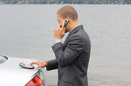 Ethnic Business Man using calculator while talking on cell phone. He is parked at the shore of the lake.
