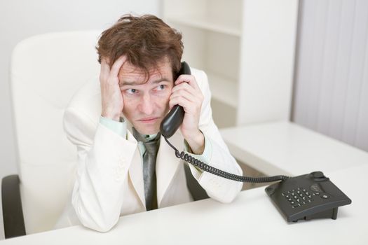 The frightened guy speaks by phone at office