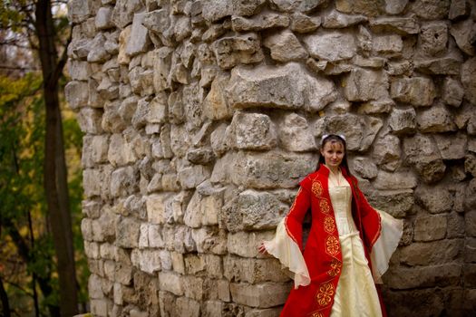 lady in medieval red dress standing near old wall
