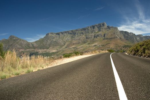 Road leading toward Table mountain in the background with blue sky and clouds