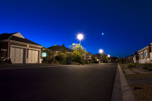 Urban night scene showing a road and various houses in a clear sky