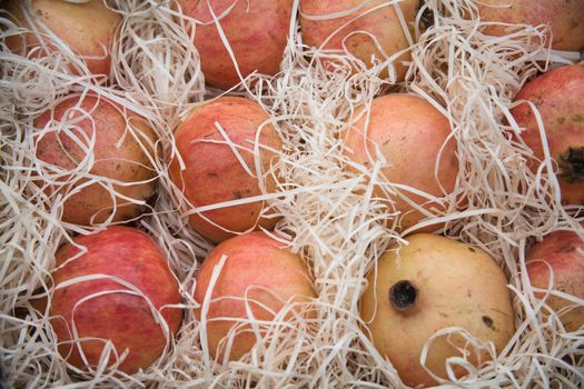 Fresh pomegranate fruits with straw on market stall.