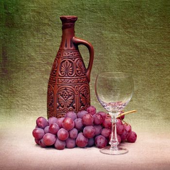 Still-life with a clay large bottle, a glass and grapes against a canvas