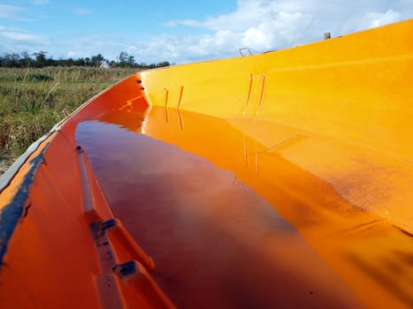 Small orange fishing skiff boat full of rain water