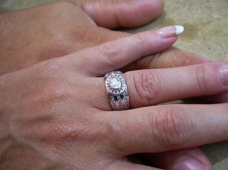 Two hands on a cement like background on top of each other showing woman's beautiful wedding ring
