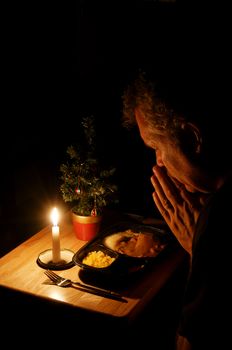 A lonely man praying over a TV dinner at Christmas.