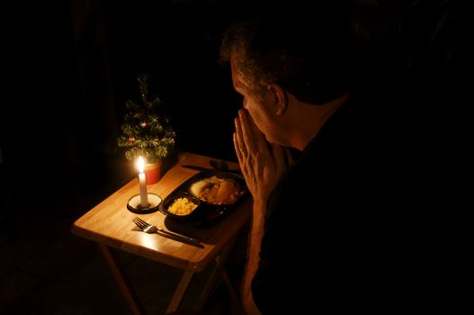 A man praying over a TV dinner at Christmas time.