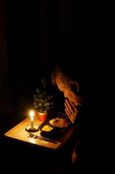 A middle-aged man praying over a TV dinner at Christmas time.