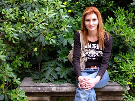 Young woman sitting on a stone bench surrounded by foliage