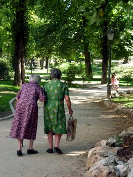 Two old age women walking on a sunny summer evening at the Retiro Park in Madrid.