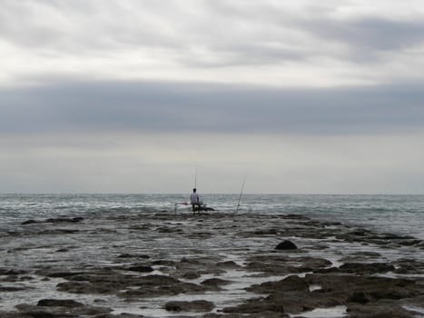 A fishermen alone at a pier in Benicasim, Spain, fishing in the sea.