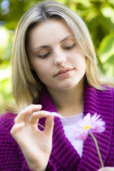 Closeup Portrait of Pretty Blond Teen Girl Looking at a Flower