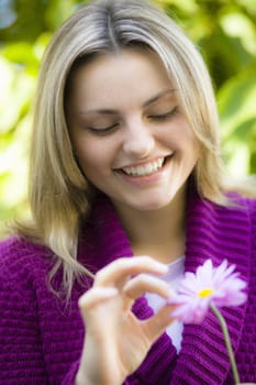 Closeup Portrait of a Smiling Pretty Blond Teen Girl Looking at a Flower
