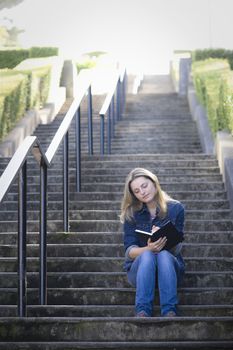 Pretty Blonde Teen Girl Sitting on a Stairway Writing in Journal