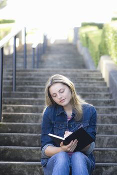 Pretty Blonde Teen Girl Sitting on a Stairway Writing in Journal