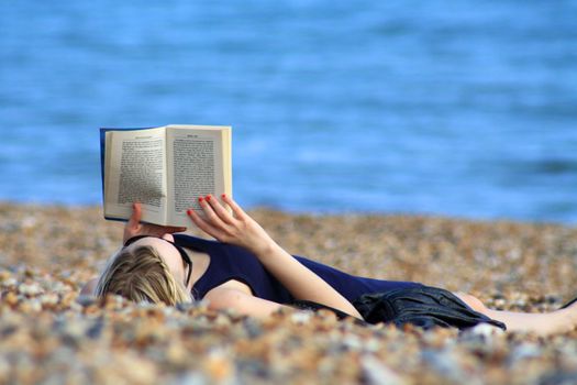 A girl reading a book on the beach.