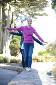 Portrait of Three Smiling Tween Girls walking along a pond while balancing and smiling.