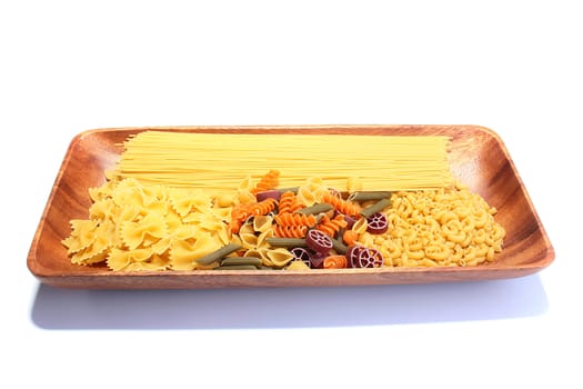 Wooden plate with different macaroni, vermicelli and a spaghetti on a white background.
