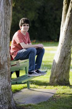 Smiling Teenage Boy Sitting on Bench in Park