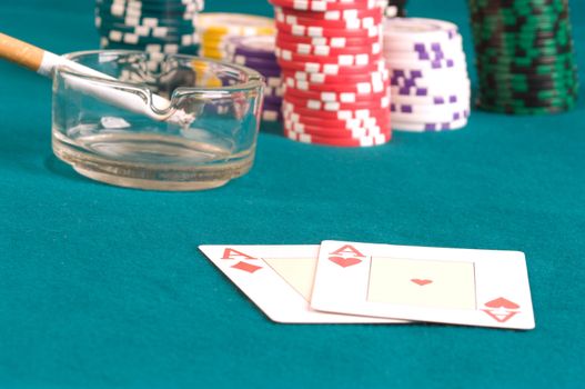 Piles of counters, an ashtray with a cigarette and playing cards on green cloth.