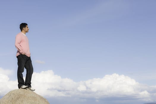 Man Standing on Rock in Front of Blue Sky and Clouds Looking into Distance