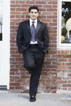 Smiling Man Dressed in Suit and Tie Leaning against Brick Wall