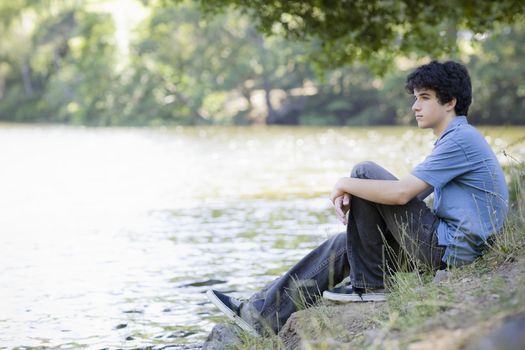 Teen Boy Sitting By lake Looking into Distance