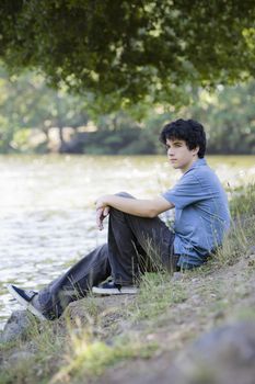 Teen Boy Sitting By lake Looking into Distance